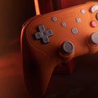 Close-up of an orange gaming controller with gray D-pad and buttons on a dark background