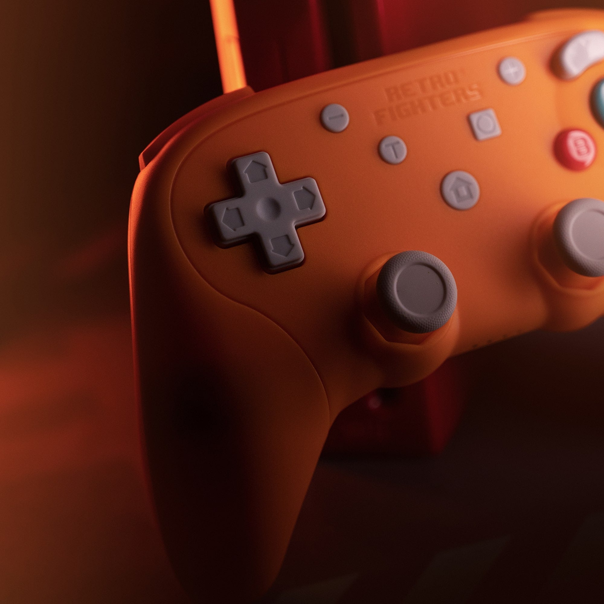 Close-up of an orange gaming controller with gray D-pad and buttons on a dark background